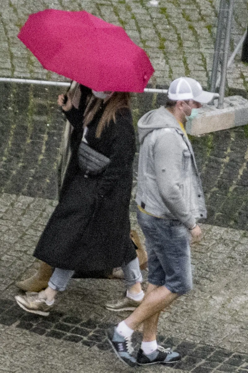 Woman under a pink umbrella walking past a man in a white cap